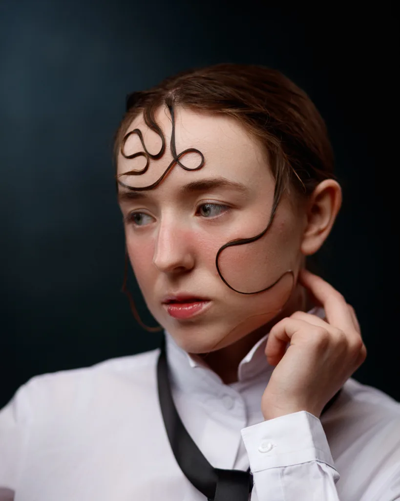 Person with artistic hairstyle and thoughtful expression.