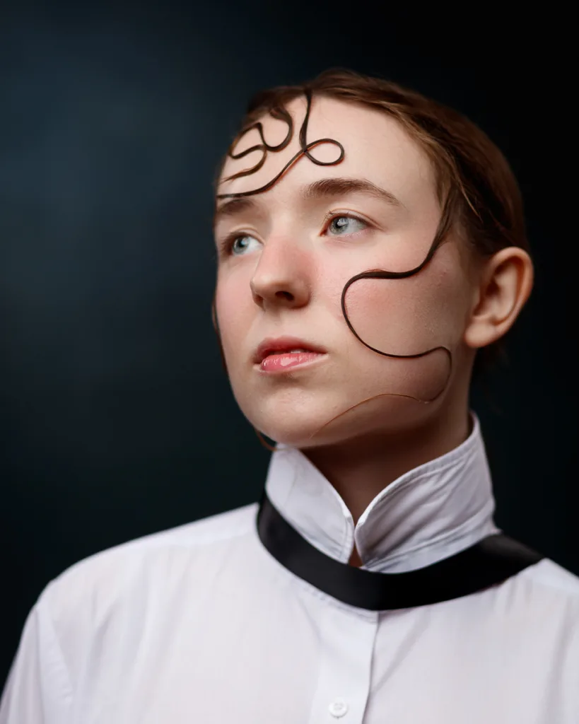Person with artistic hairstyle, wearing a high-collared shirt.