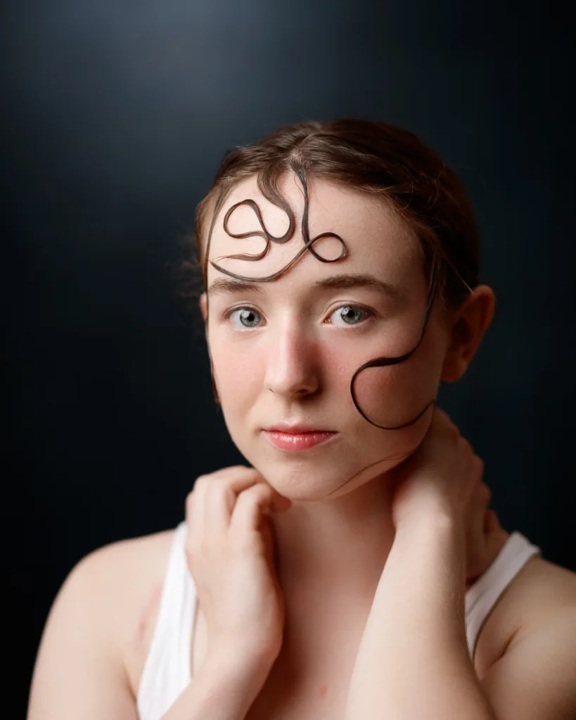 Model with styled hair on face, dark background.