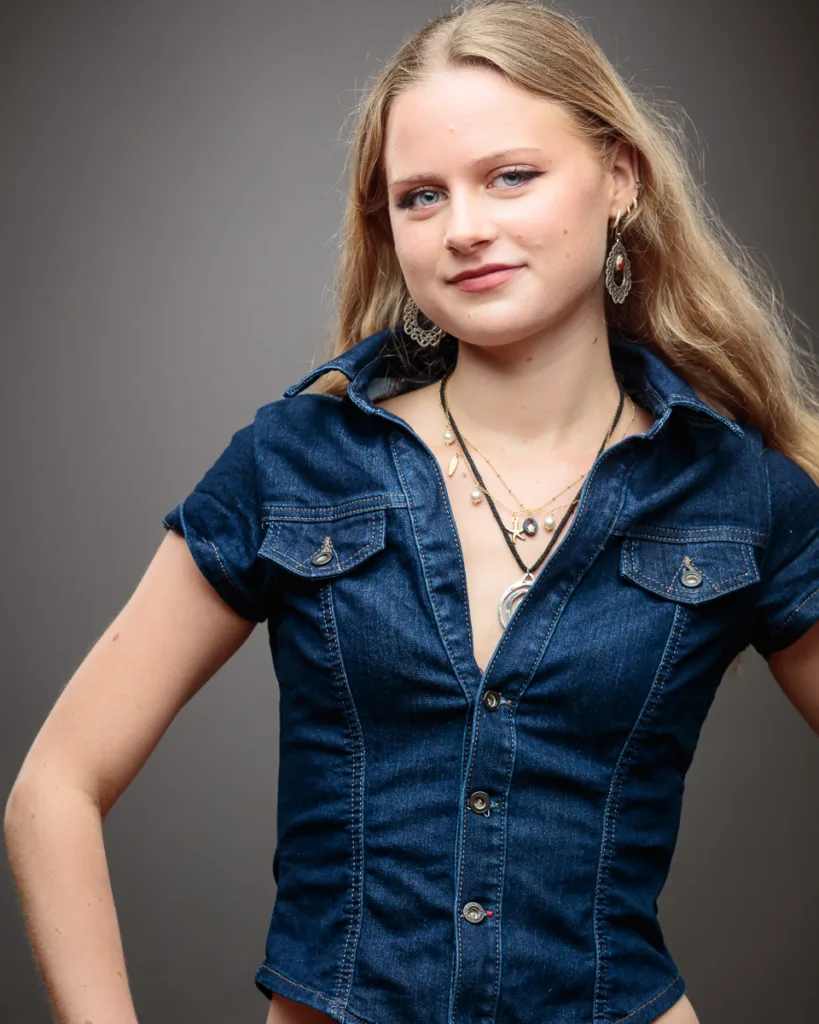 Woman in denim shirt with layered necklaces.