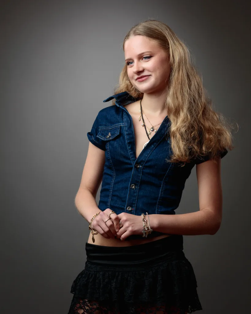 Woman in denim top posing against grey background.