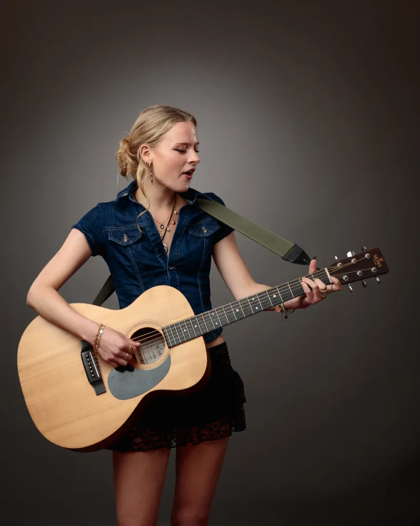 Woman playing acoustic guitar, singing passionately.