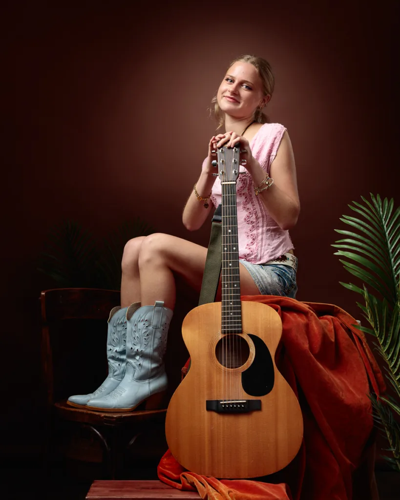 Person sitting with guitar and wearing boots indoors.