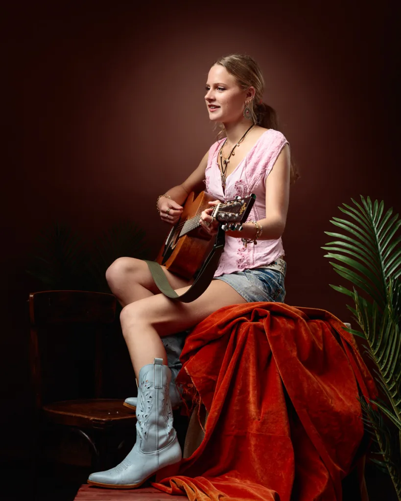 Woman playing guitar, casual attire, brown background.