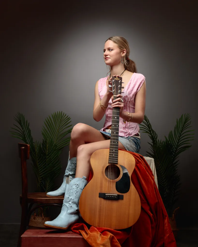 Woman sitting with acoustic guitar, wearing blue boots.