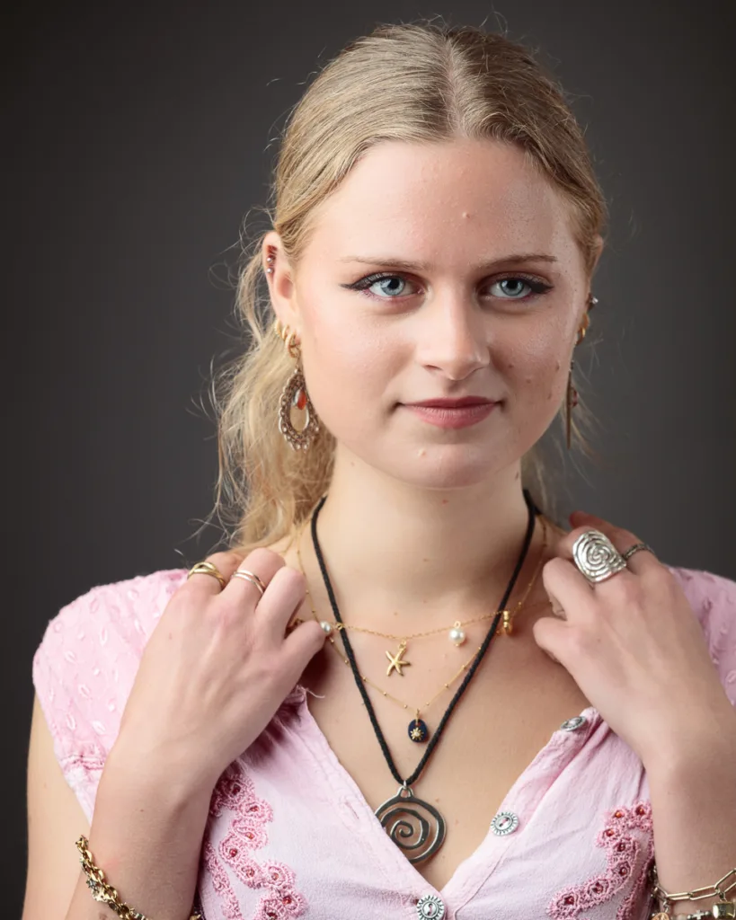 Woman wearing layered necklaces and earrings, dressed in pink.