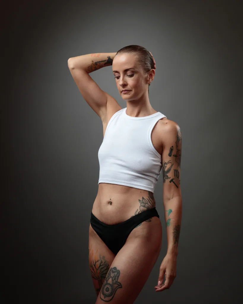 Tattooed person posing in white top and black bottoms.