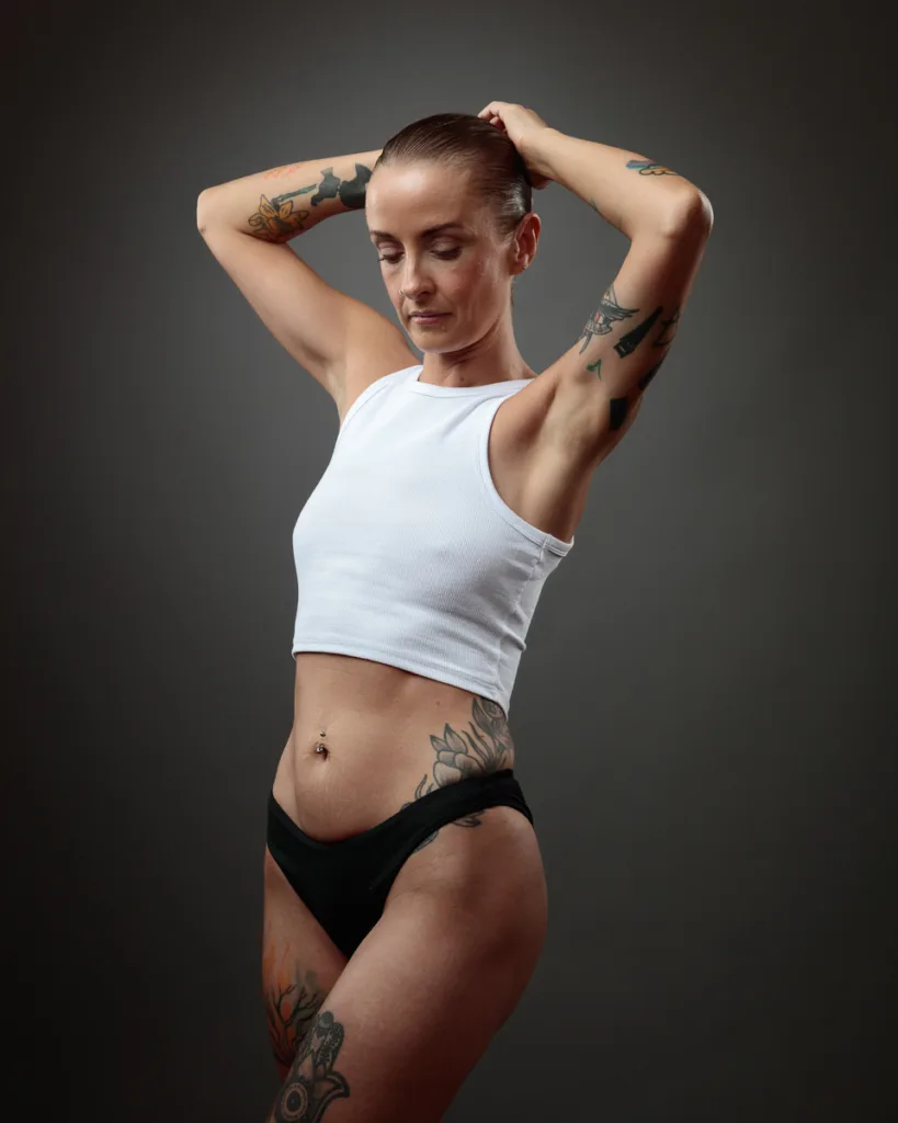 Tattooed woman in white tank top poses confidently.