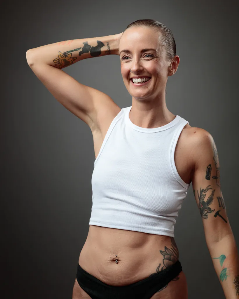 Smiling person with tattoos wearing white tank top.