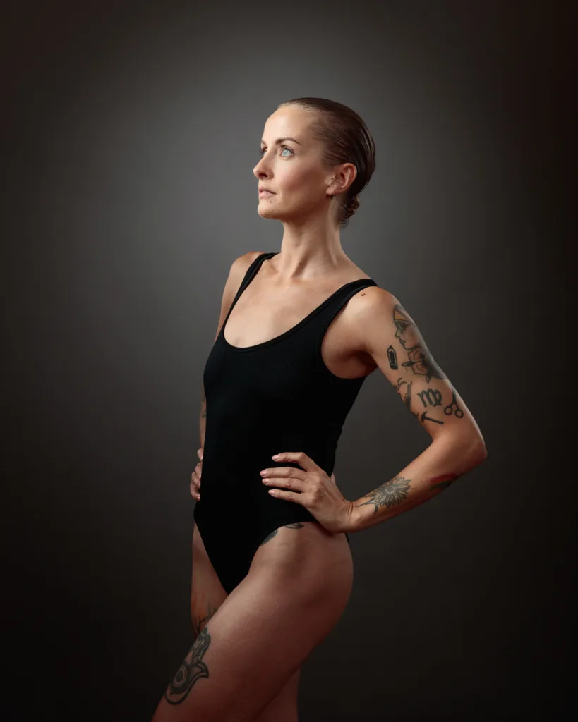 Woman with tattoos in black swimsuit posing sideways.