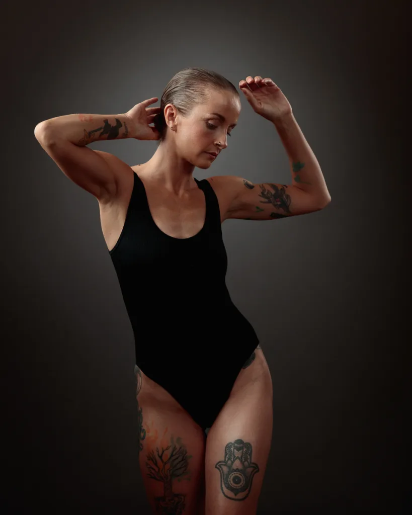 Tattooed woman in black bodysuit posing elegantly.