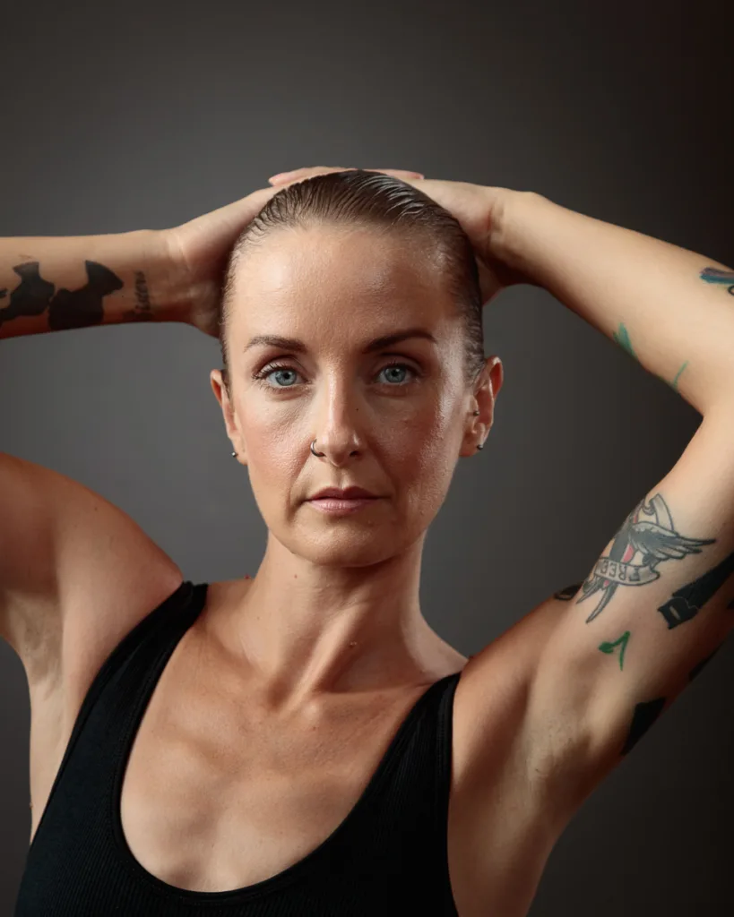 Person with tattoos posing confidently against grey background.