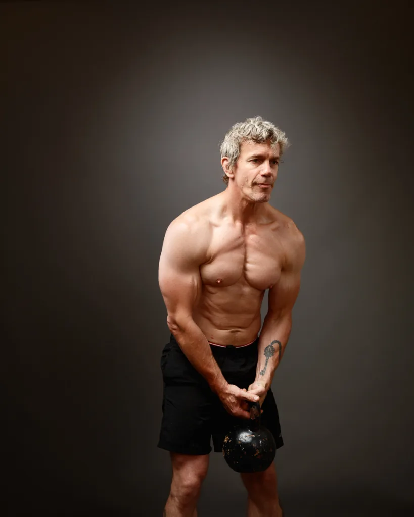 Shirtless man exercising with kettlebell.