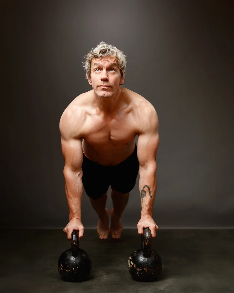 Man doing push-up on kettlebells, studio background.