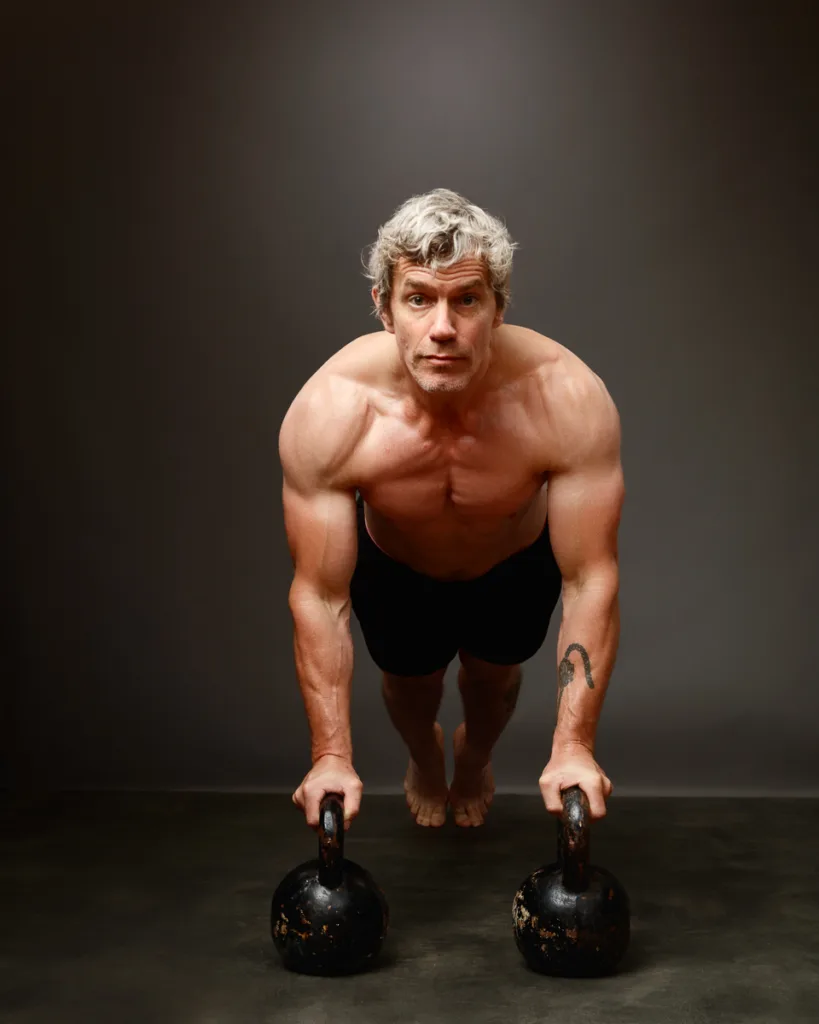 Man exercising with kettlebells in push-up position.