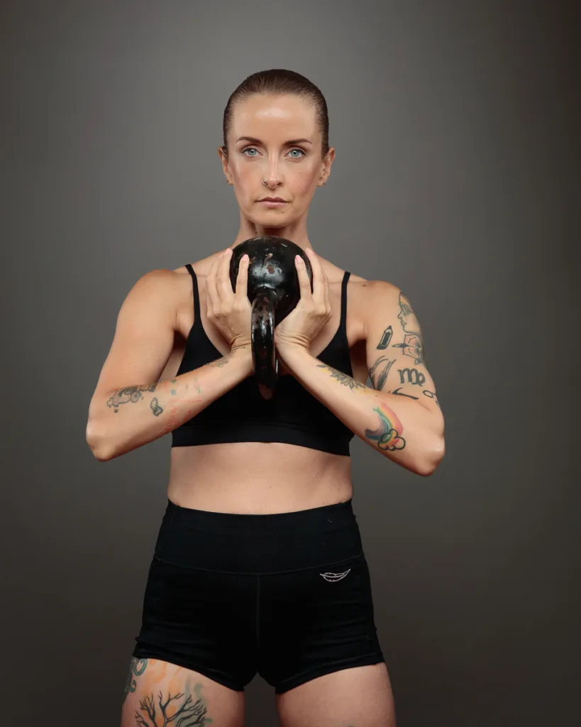 Woman holding kettlebell, showing strength and tattoos.