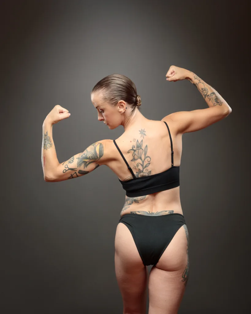 Woman flexing muscles, showing tattoos on her back.