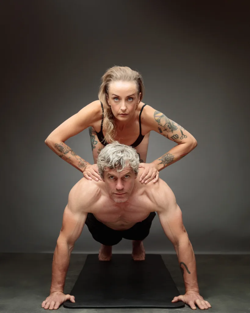 Couple doing acro yoga pose on black mat.