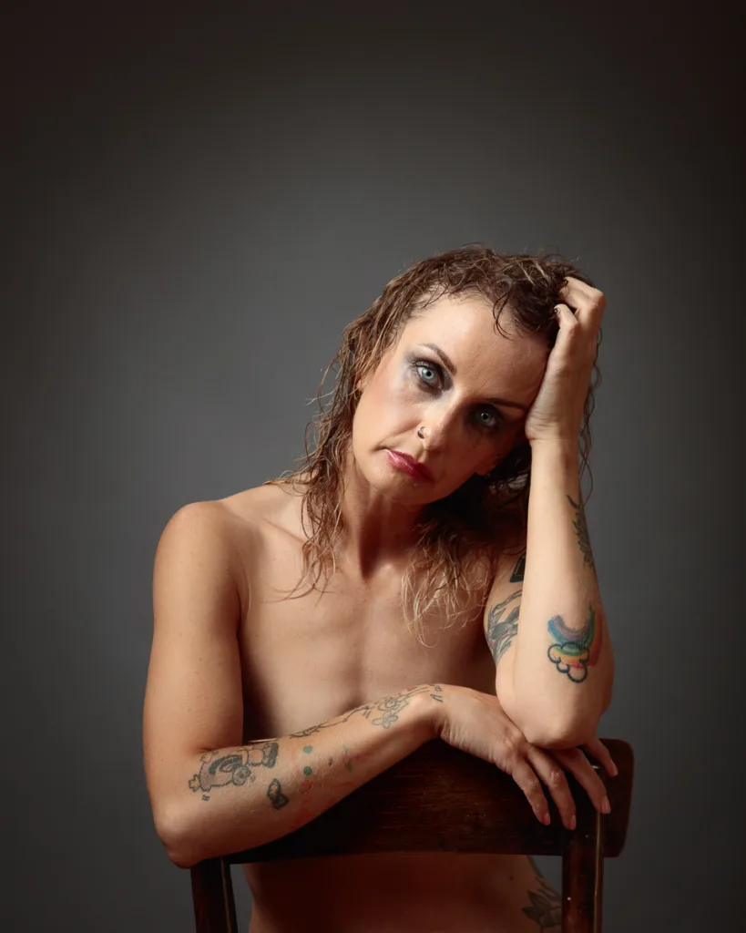 Tattooed woman sitting on chair, moody expression