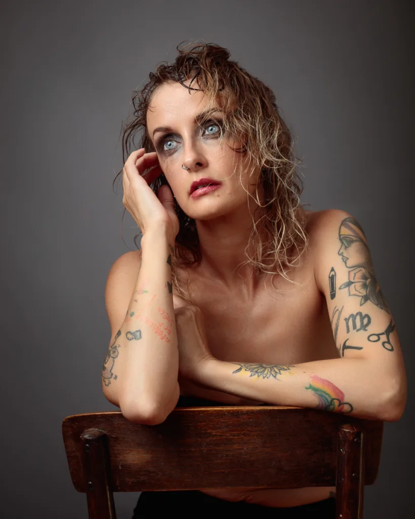 Tattooed woman with wet hair sitting on chair.