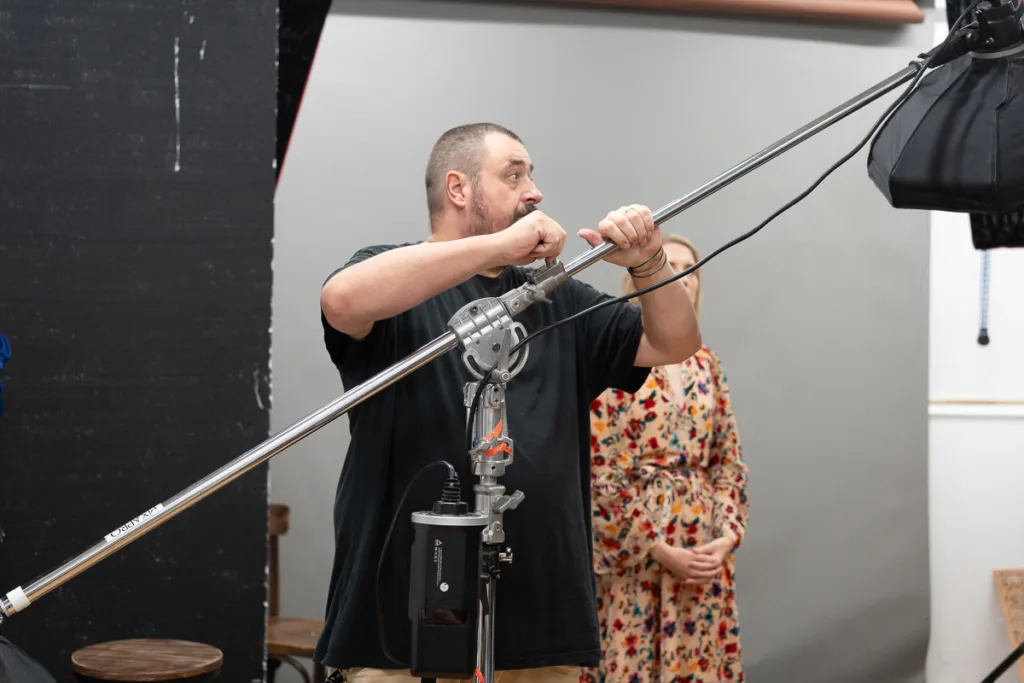 Man adjusts studio lighting equipment in photoshoot setting.