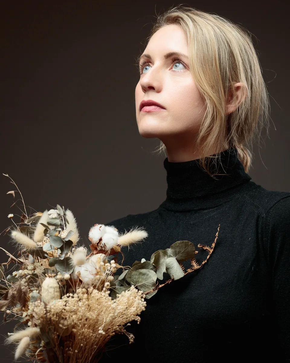Woman holding dried floral arrangement, black turtleneck.