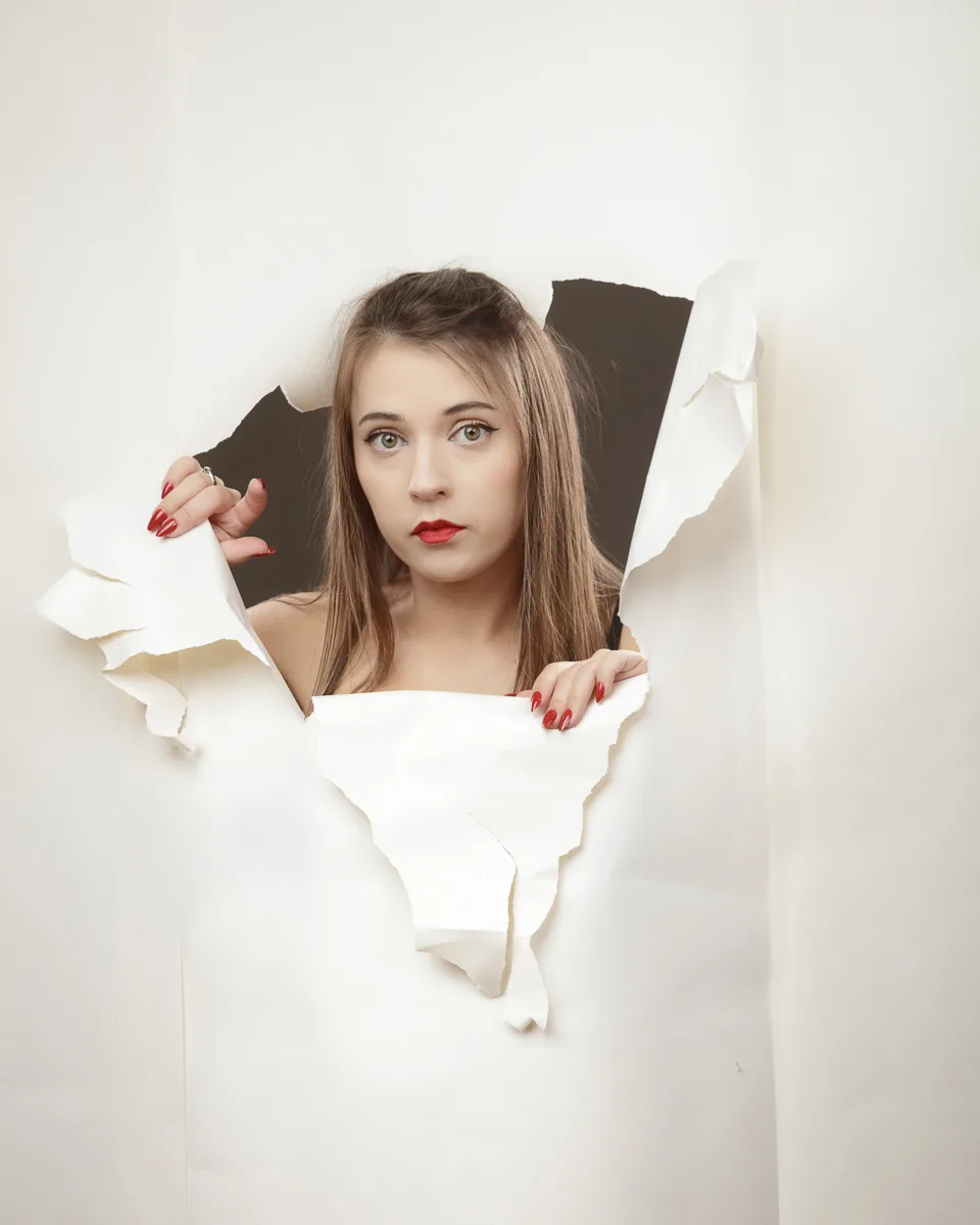Person emerging through torn white paper background.