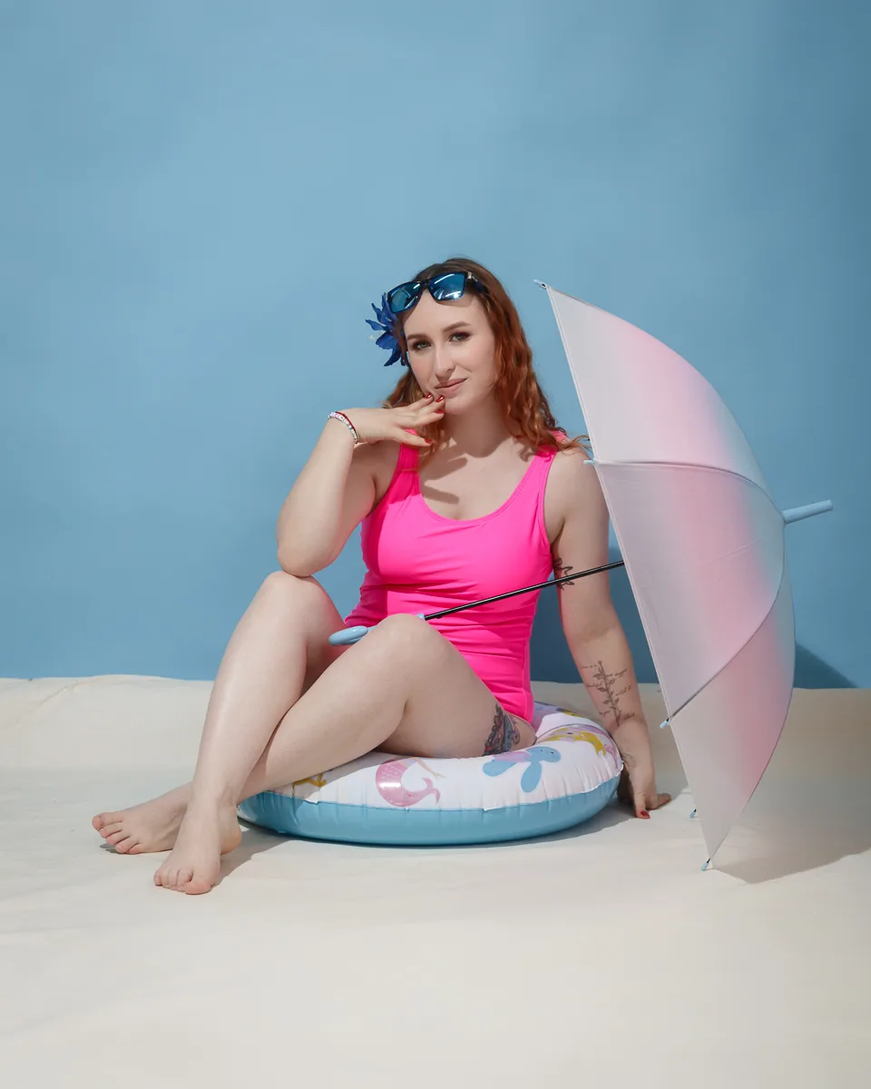 Woman in pink swimsuit with umbrella posing indoors