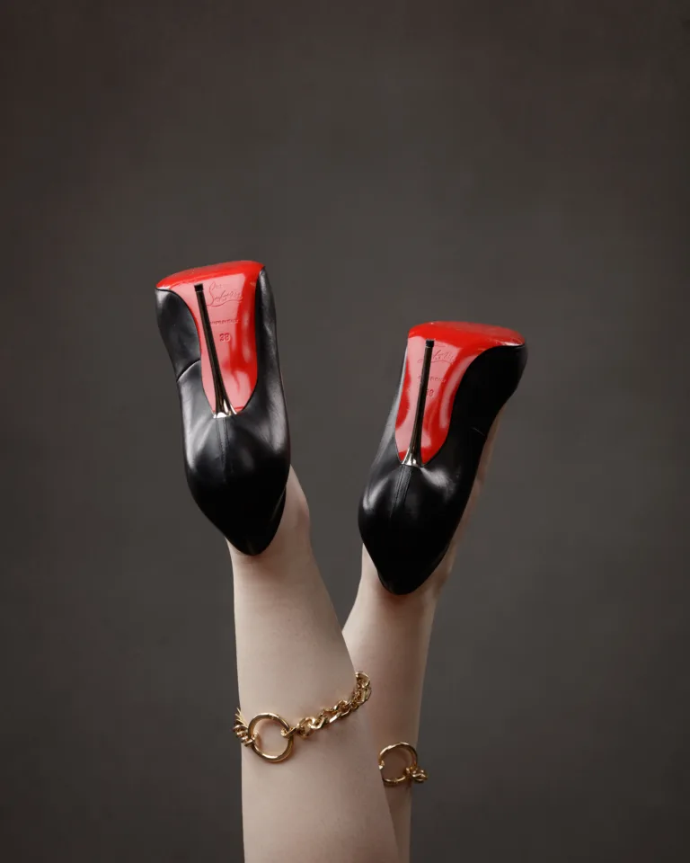 Red-soled black high heels on legs with bracelets.