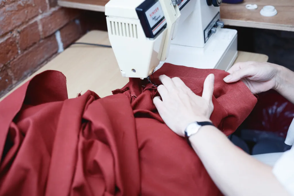 Person sewing red fabric with a machine.