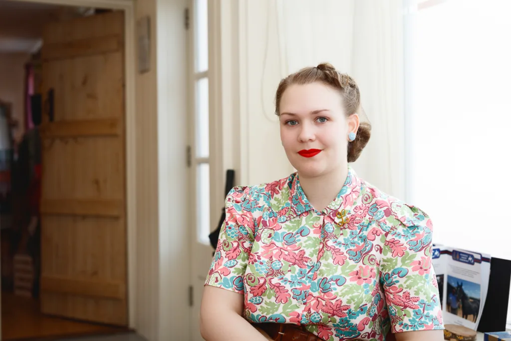 Woman in floral dress, red lipstick, indoors.