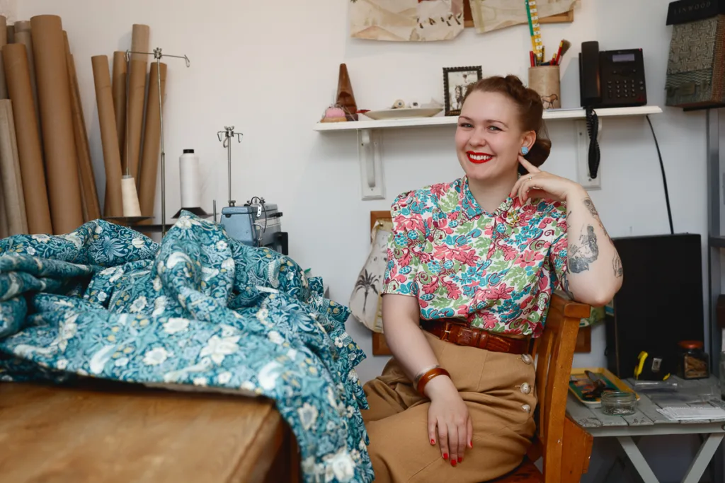Smiling woman in floral shirt, sitting by fabric.