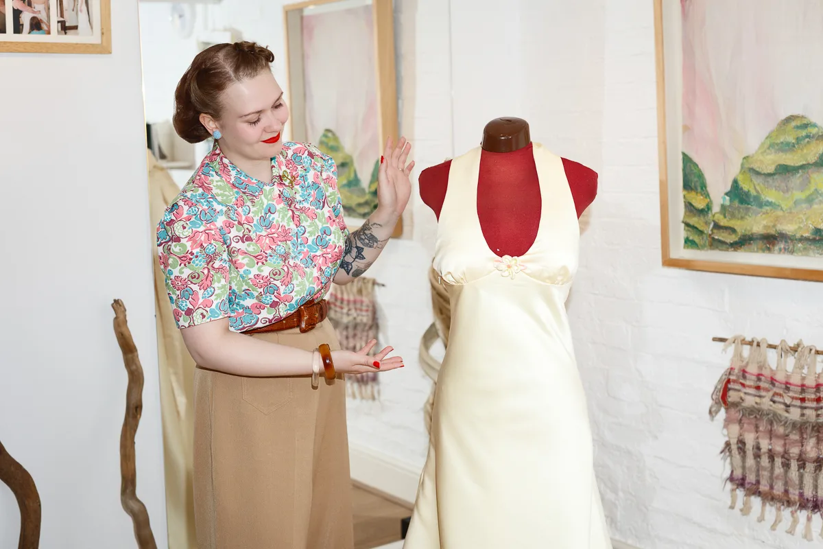 Woman showing vintage dress on mannequin in shop.