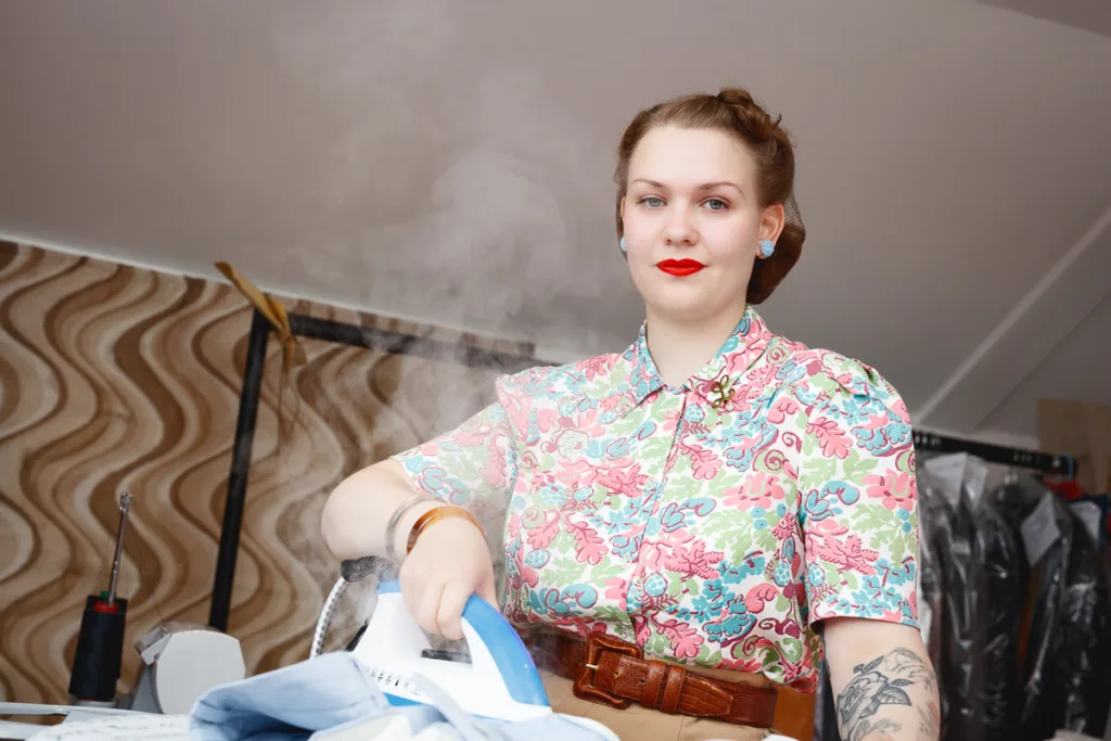 Woman ironing clothes in retro-patterned blouse.