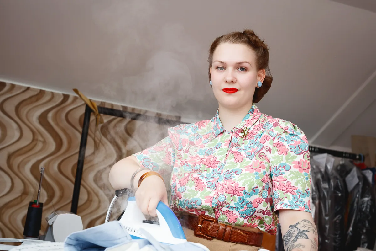Woman ironing clothes in retro-patterned blouse.