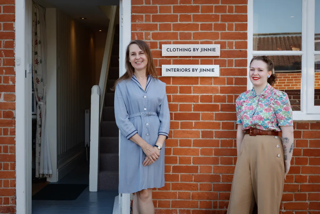 Two women outside boutique with 'By Jinnie' sign.