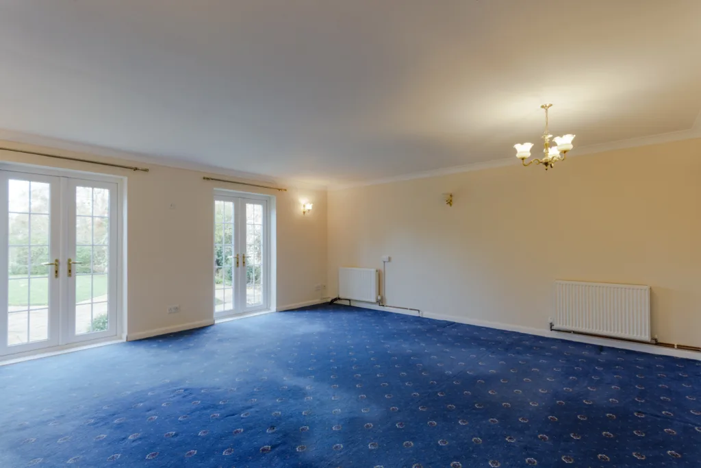 Spacious carpeted room with French doors and chandelier.