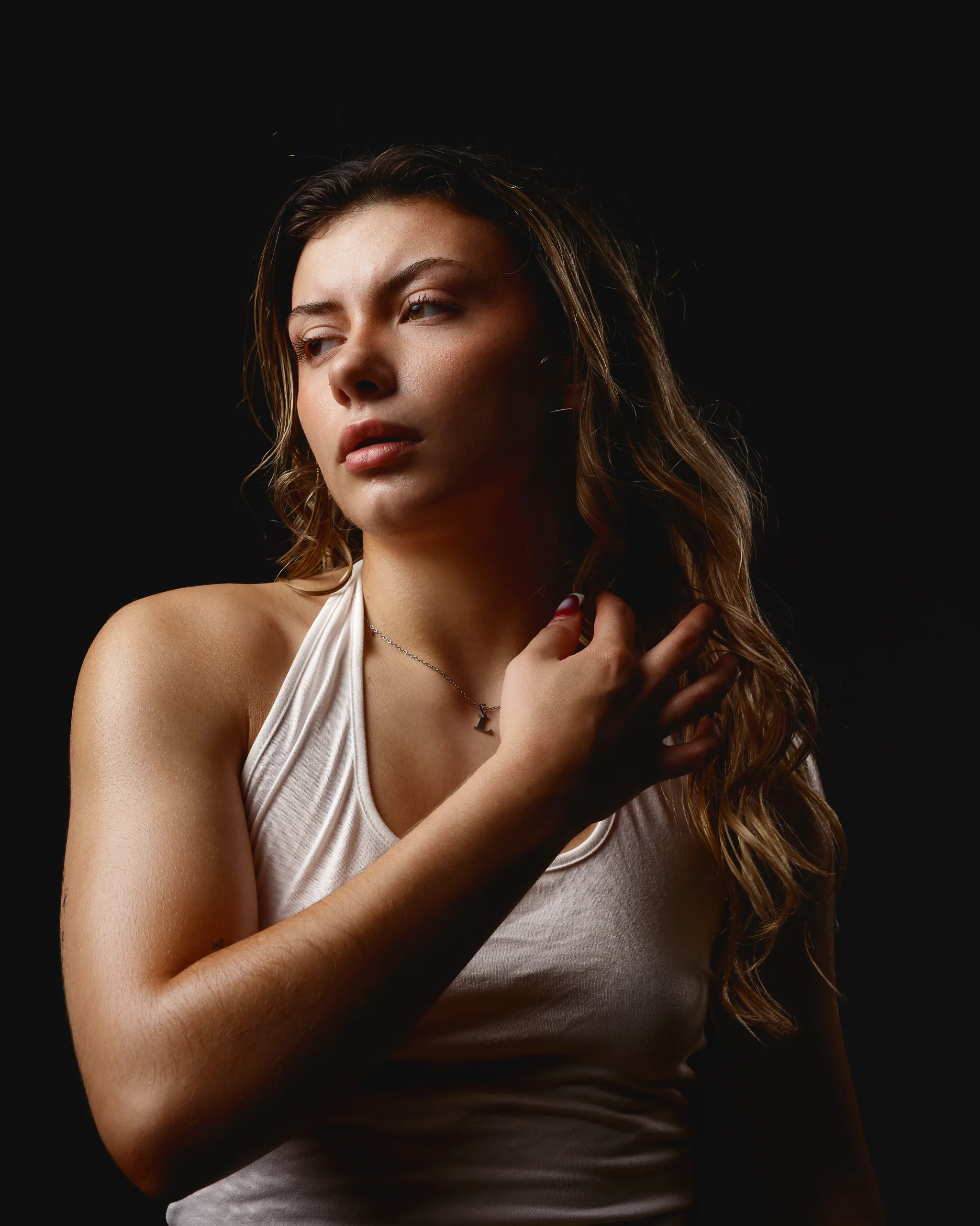 Woman posing in dramatic lighting wearing white top.