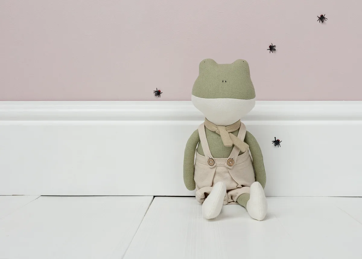 Stuffed frog toy with flies on pink wall.