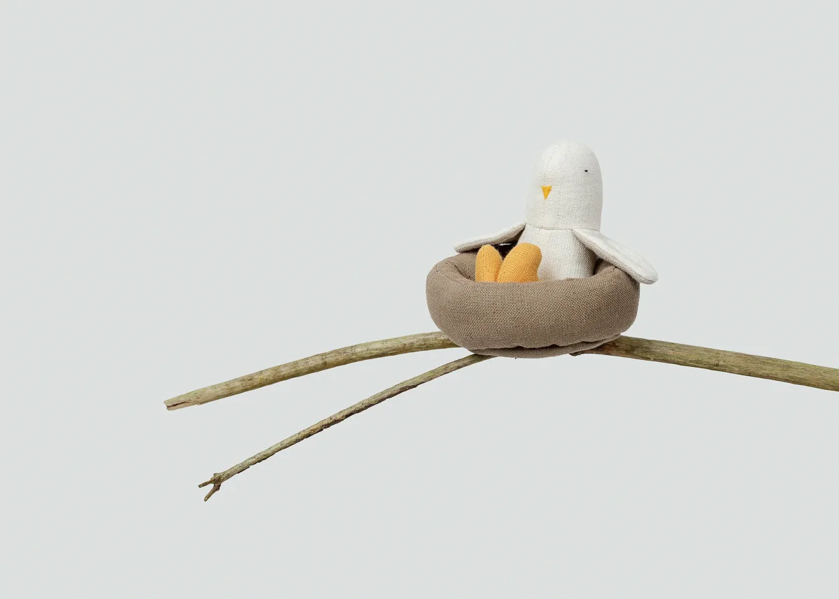 Stuffed bird toy in nest on branch.