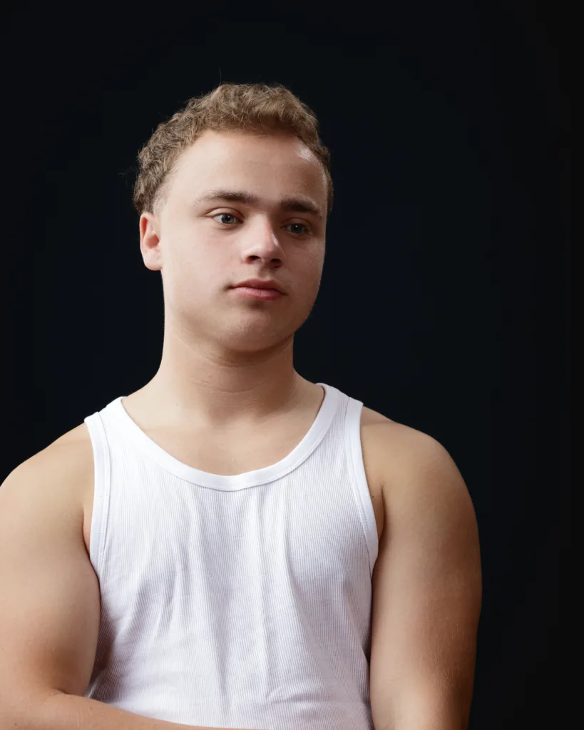 Person in white vest against dark background.