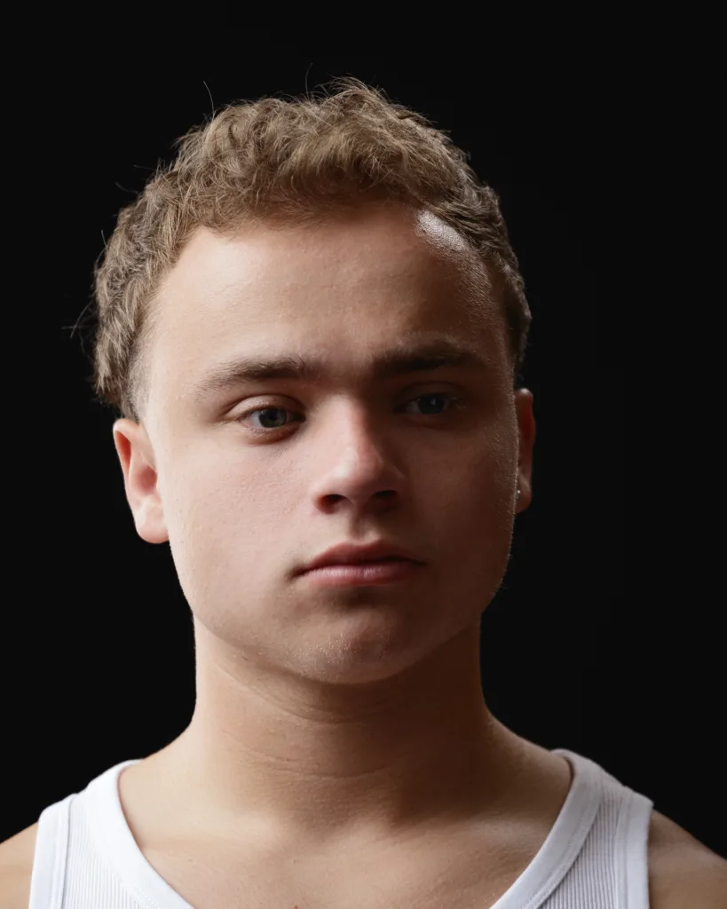 Young man in white tank top against black background.