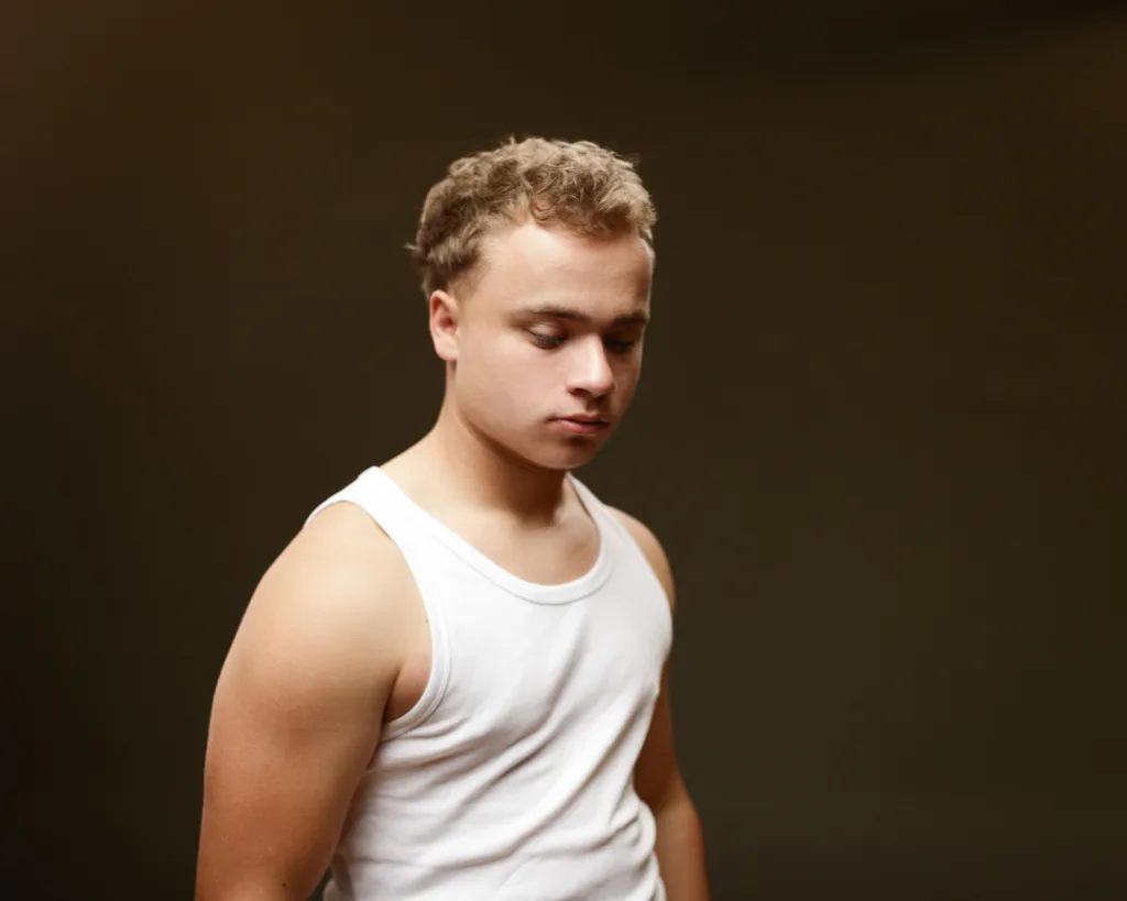 Person in white vest, pensive expression.