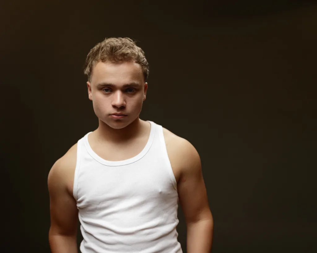 Man in white tank top, dark background.