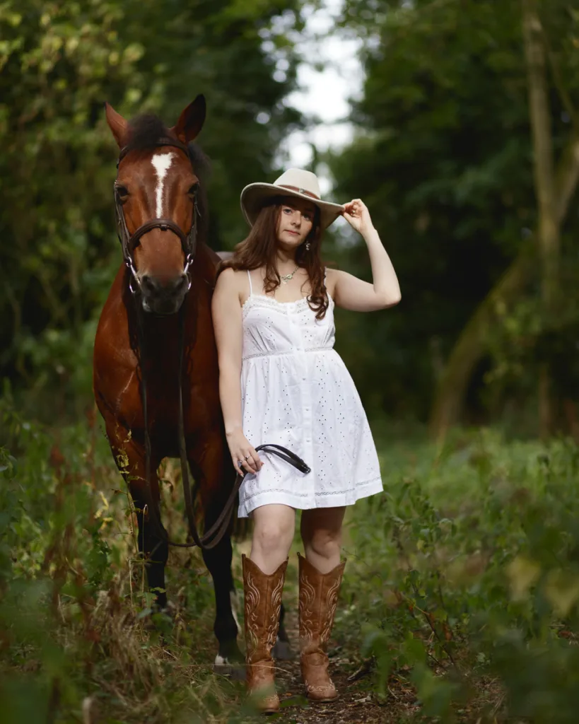 Woman in white dress with horse in forest.