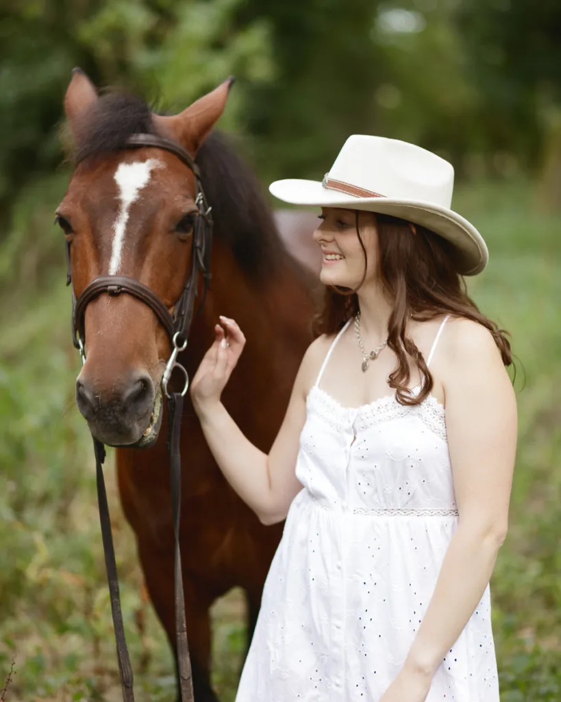 Woman in hat petting horse in forest