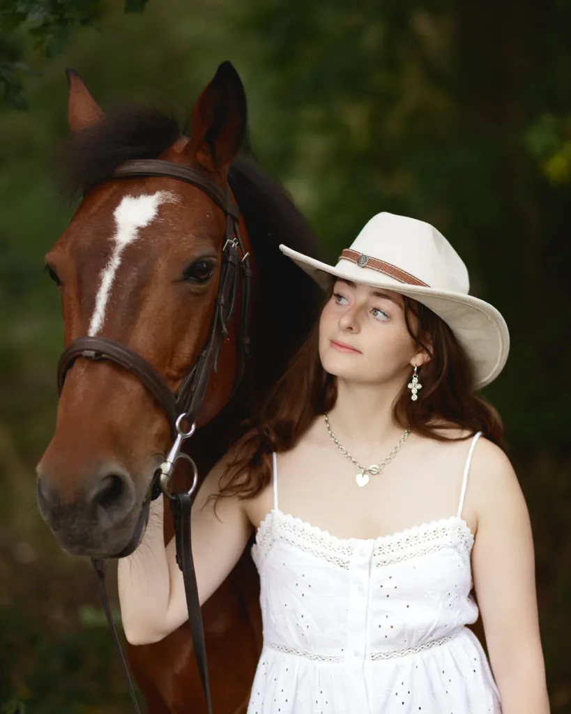 Woman in white dress with brown horse outdoors.