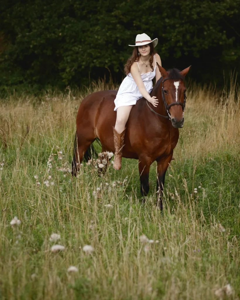 Woman riding horse in grassy field, wearing hat.