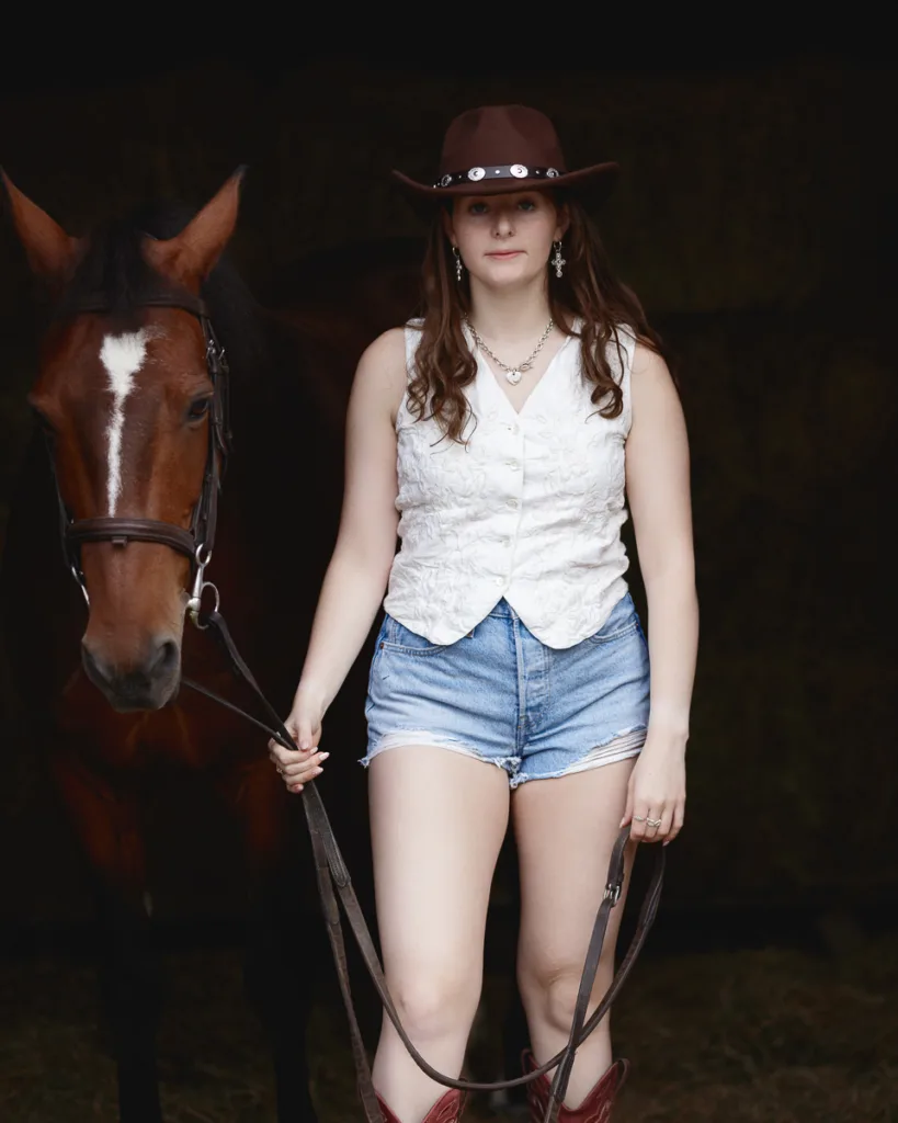 Woman in cowboy attire with a horse.