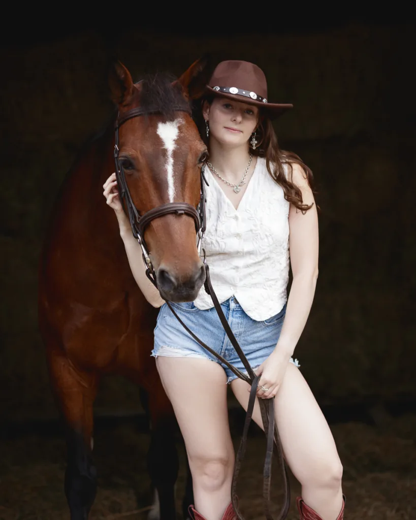 Woman in cowboy hat with horse, wearing denim shorts.
